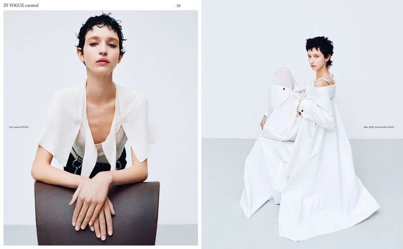 Fashion editorial shot in a studio setting, showcasing a model wearing a white top and black bottoms and another sitting in white clothing.