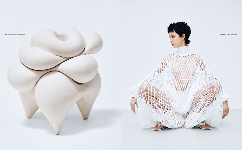Woman in white net dress sits near sculpted stool in a minimalist white setting, modern fashion editorial with artistic design elements.