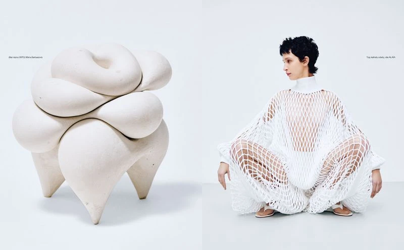 Woman in white net dress sits near sculpted stool in a minimalist white setting, modern fashion editorial with artistic design elements.
