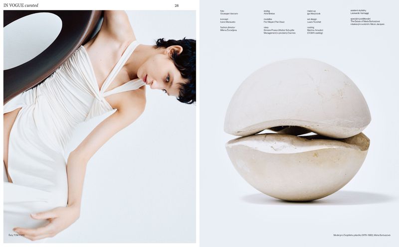 Fashion editorial shot featuring a model in a white dress leaning against a dark wood chair, contrasted with a sculptural white object.