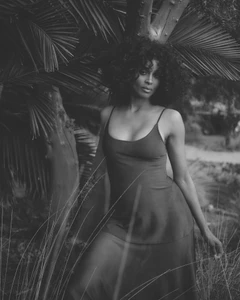 Ciara posing among palm fronds and tropical foliage wearing a dark slip dress in a black and white editorial portrait.