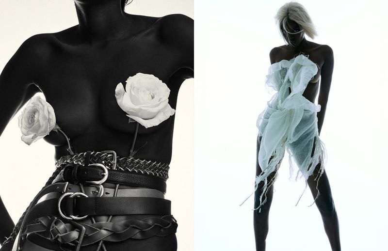Two women strike poses in a studio setting; one wears belts and roses, while the other is adorned with sheer white fabric.