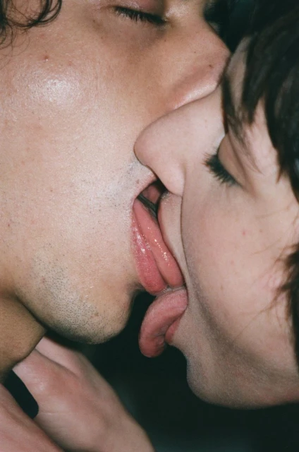 Close-up of two adults in a close embrace; their faces nearly touching, lips slightly parted showing tongues, in a tight, intimate moment.
