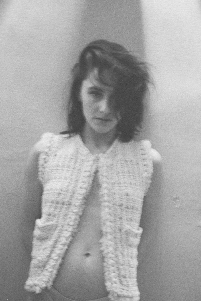 Monochrome portrait of an adult woman with dark hair wearing a textured sleeveless top, posing against a light grey wall.