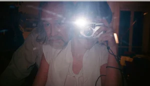 Two people taking a mirror selfie with a flash camera, casting a bright glare in an indoor room