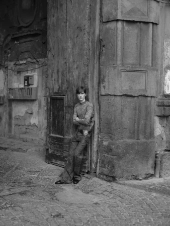 Young man in patterned sweater poses against weathered stone wall and arched doorway in black and white, creating a vintage street style.