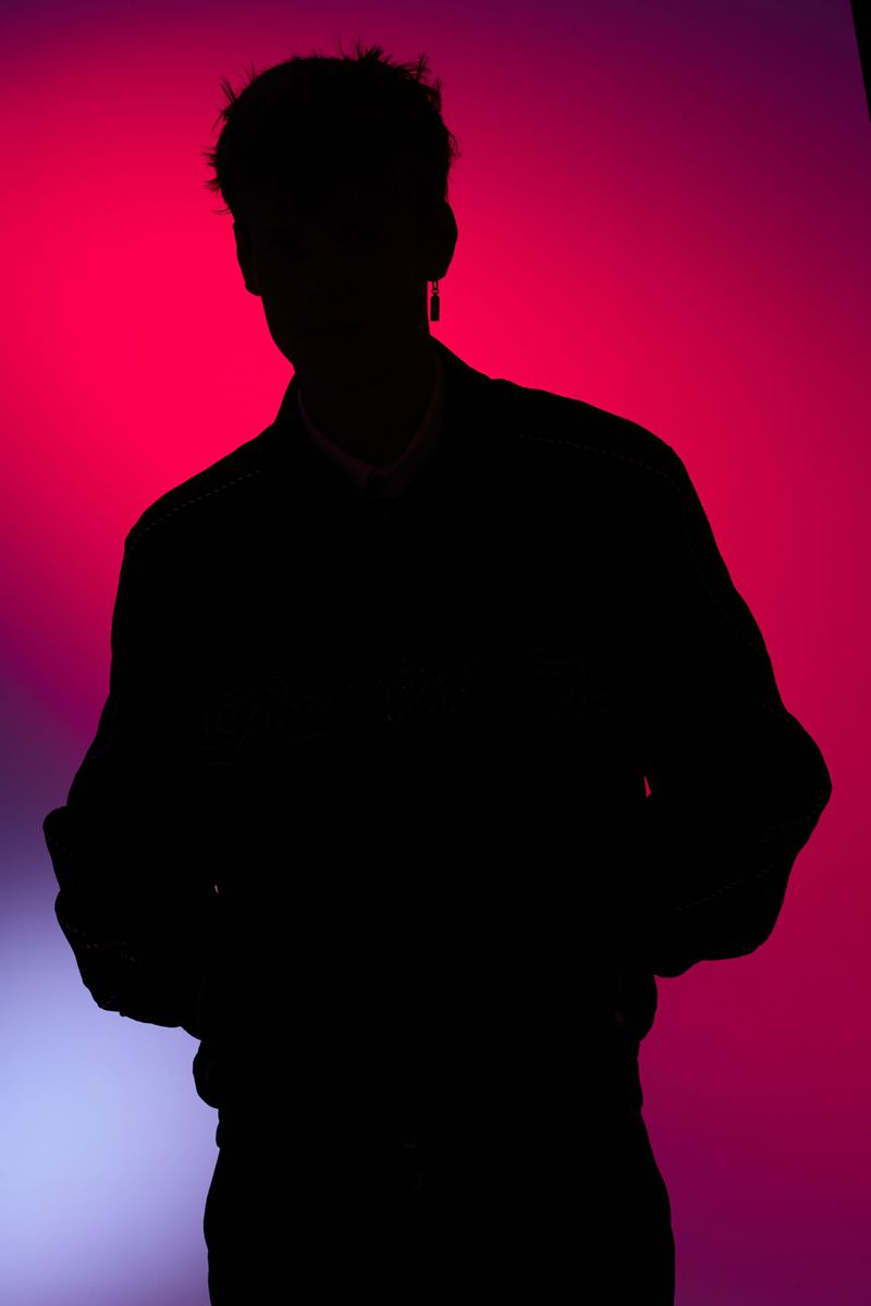 Silhouette of an adult male in a dark jacket against a vibrant, gradient background of red and blue tones in a studio setting.