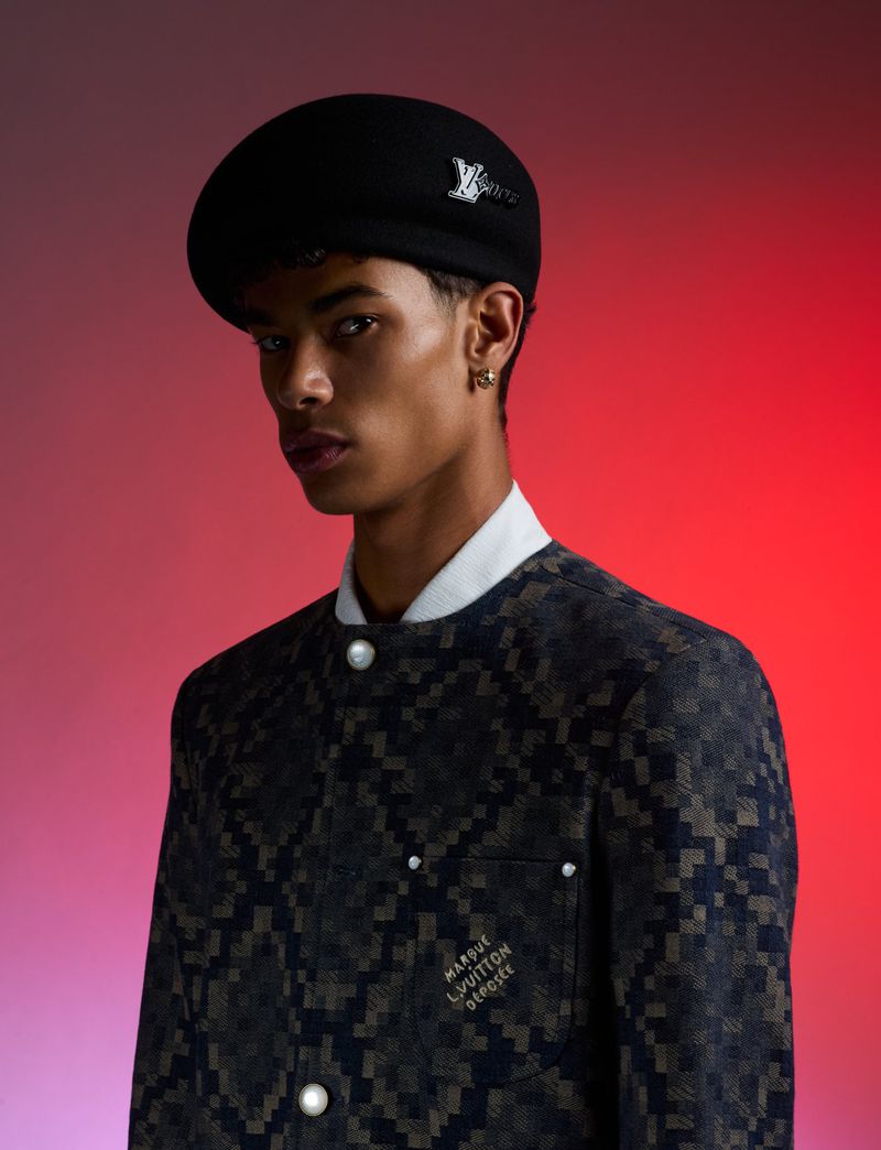 Portrait of a handsome adult male with a black beret and patterned jacket, posing in front of a gradient red background.