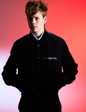Young male model wearing a black bomber jacket against a vibrant red gradient background for At Large Magazine.
