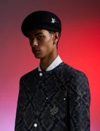 Model wearing a black beret with silver insignia and a dark patterned jacket against a red and purple gradient background.