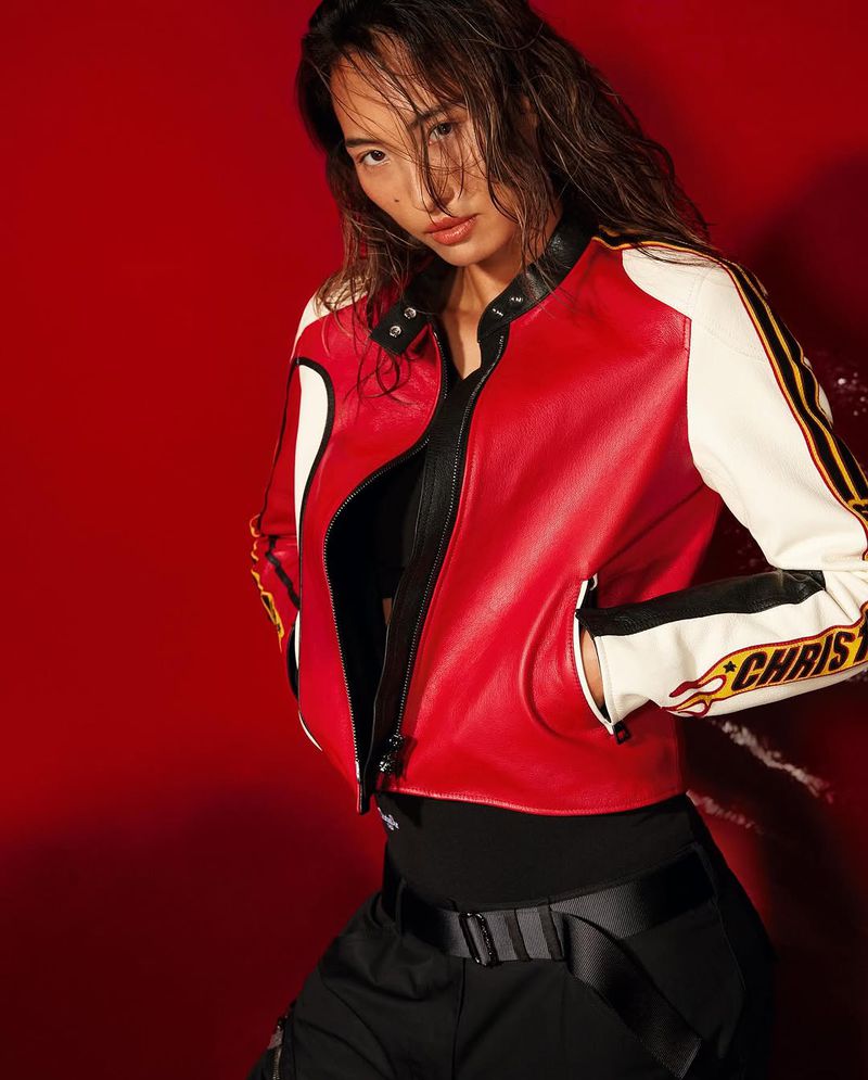Woman poses in a red and white leather jacket with flame details against a matching red background in a fashion forward studio shot.
