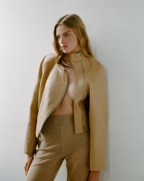 Model Eduarda Bretas wearing a tan jacket and matching trousers against a plain white studio wall for Citta Bella.