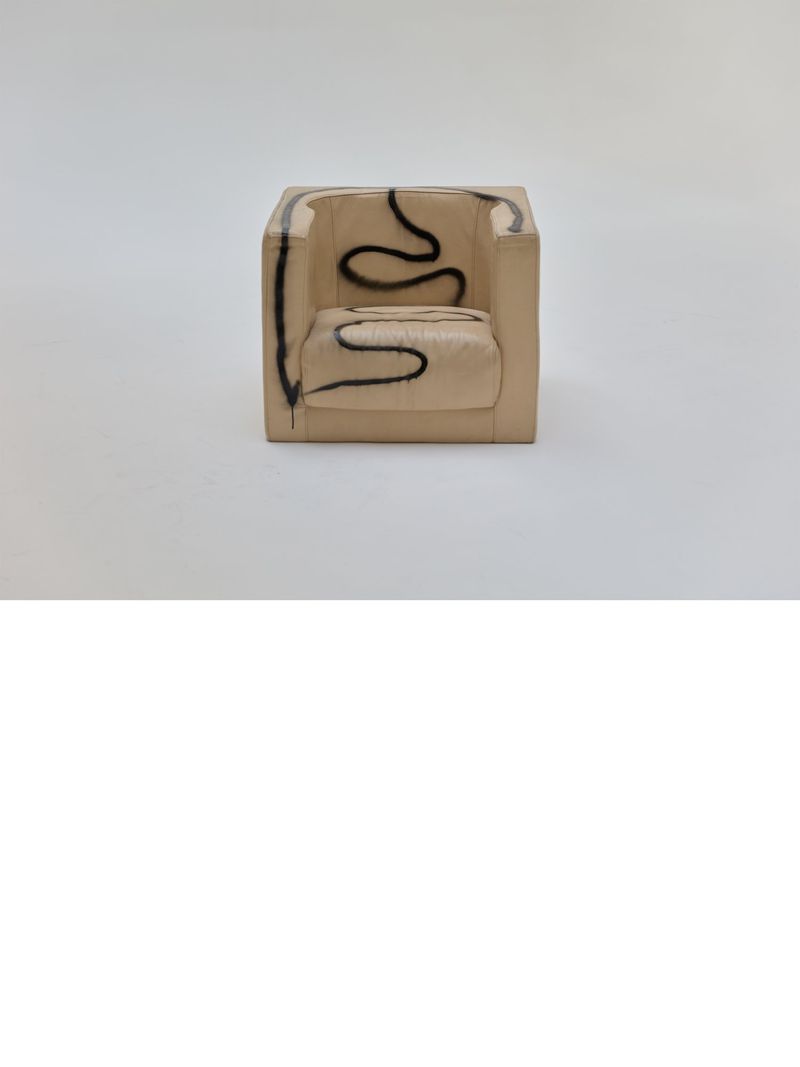 Modern square armchair upholstered in beige fabric with black graffiti-style line art sits centered on a white studio background.