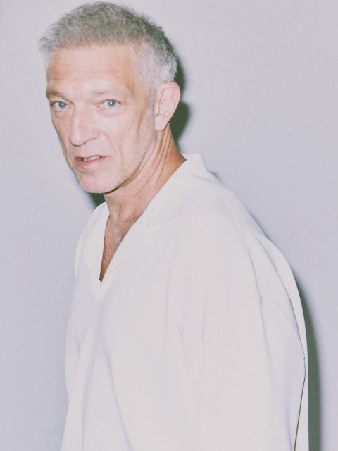 Portrait of an adult male with short grey hair, wearing a white shirt, shot in a photo studio with a neutral background.