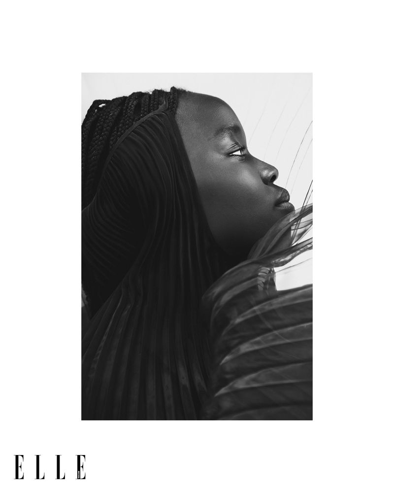 Black and white portrait of a young woman with braided hair wearing a pleated garment, shown in profile with bright, even lighting.