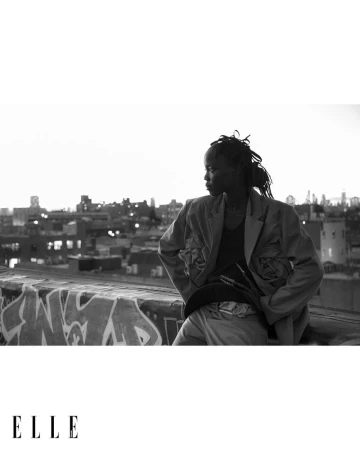 Model wearing an oversized jacket against a rooftop city skyline background in a black and white fashion photograph