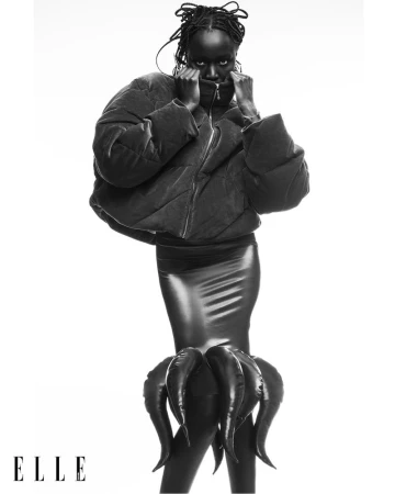Monochrome fashion shot: Black woman in a puffer jacket and octopus skirt posing against a white backdrop for Elle magazine.