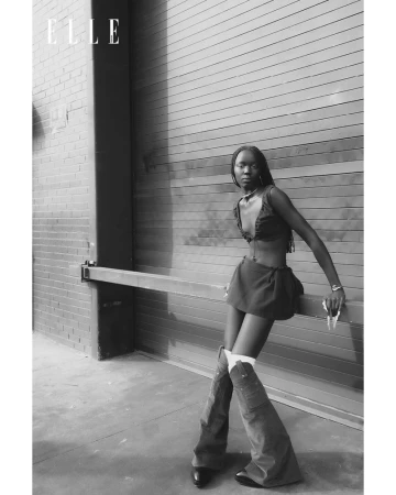 Monochrome fashion portrait of a model leaning against a ribbed metal industrial door wearing a two piece outfit and tall boots