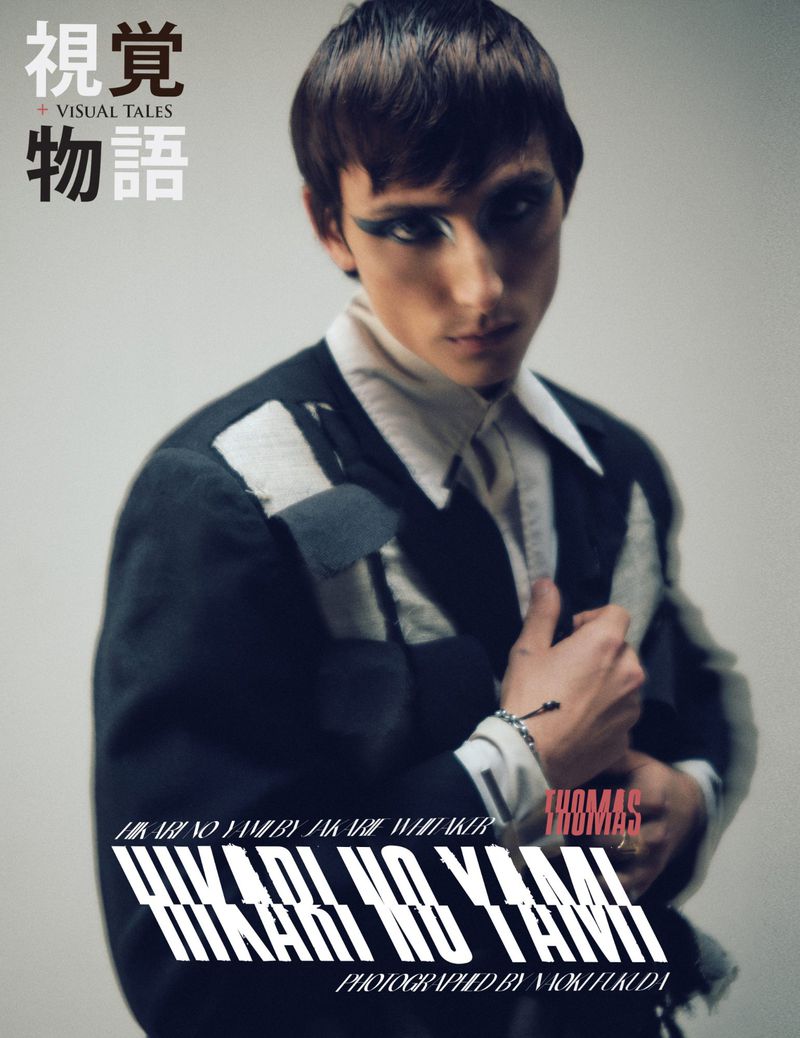 Fashion portrait of a young adult with dark eye makeup and short hair, wearing a blazer in a studio setting with visual text.