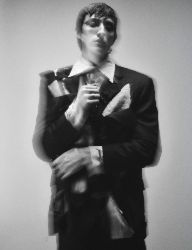 Model in dark suit jacket with motion blur holding clothing against a plain background for Visual Tales