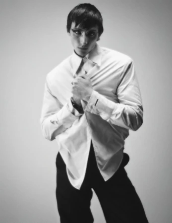 Monochrome portrait of a male model in a white button-down shirt and dark trousers against a plain background.
