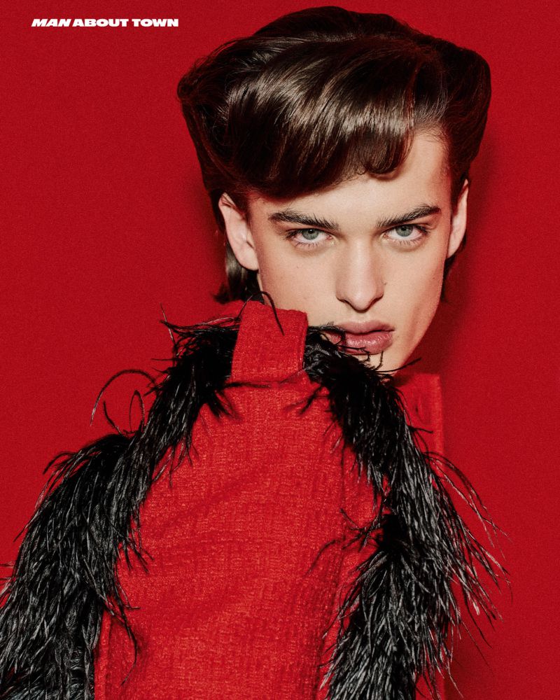 Close-up studio portrait of a young adult male wearing a red top with black feather boa, against a solid red backdrop.