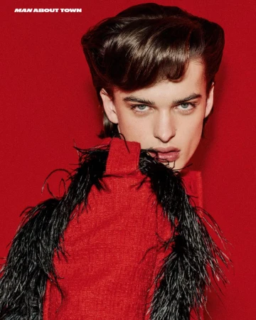 Close-up studio portrait of a young adult male wearing a red top with black feather boa, against a solid red backdrop.