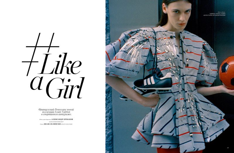 Model wearing a striped, embellished structured peplum jacket holding a red soccer ball in a magazine editorial layout