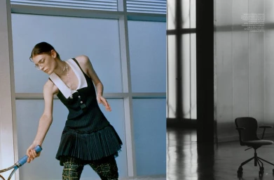 Model wearing a dark sleeveless dress with a white collar holding a tennis racket against an architectural blue background