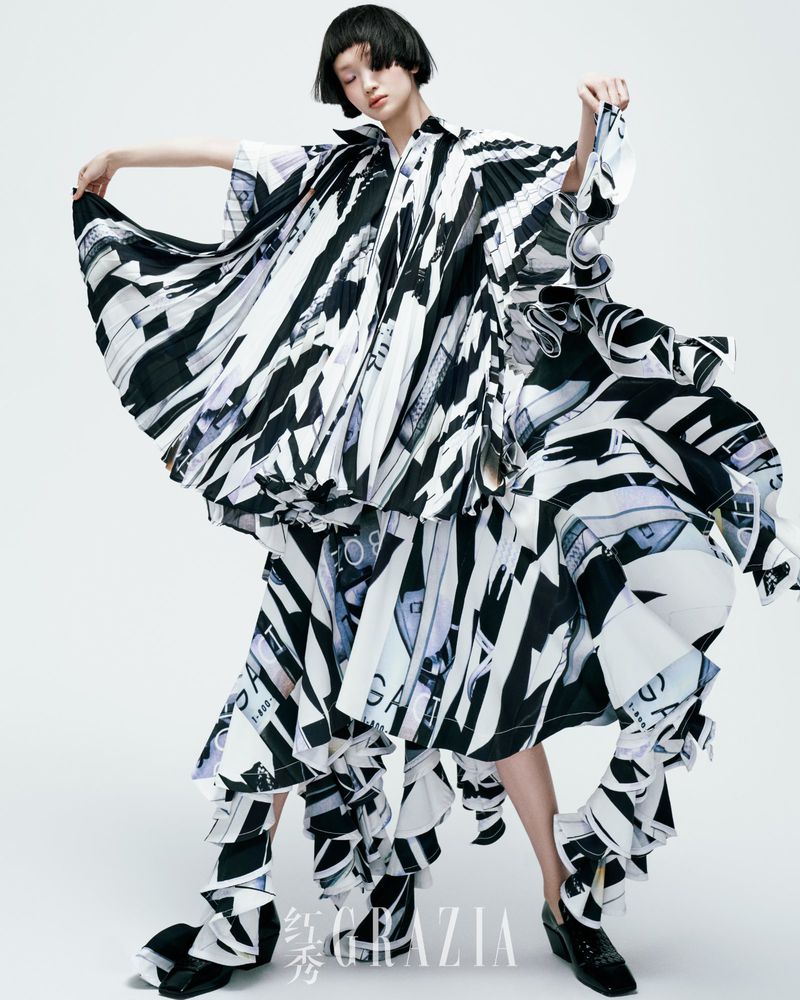 Fashion editorial shot of a model in a striking black-and-white patterned dress against a seamless white backdrop, showcasing a unique style.