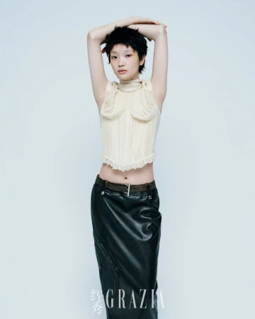 Full-length portrait of a young, slender woman with short black hair in a cream-colored top and black skirt posing in a photo studio.