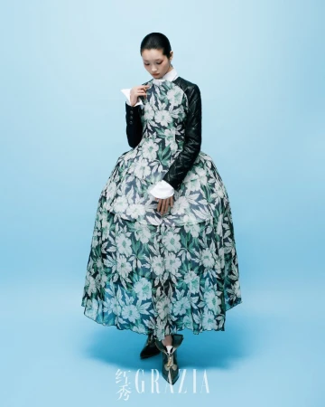 Fashion model poses in a floral gown with black leather sleeves against a light blue backdrop in a studio, showcasing contemporary fashion.