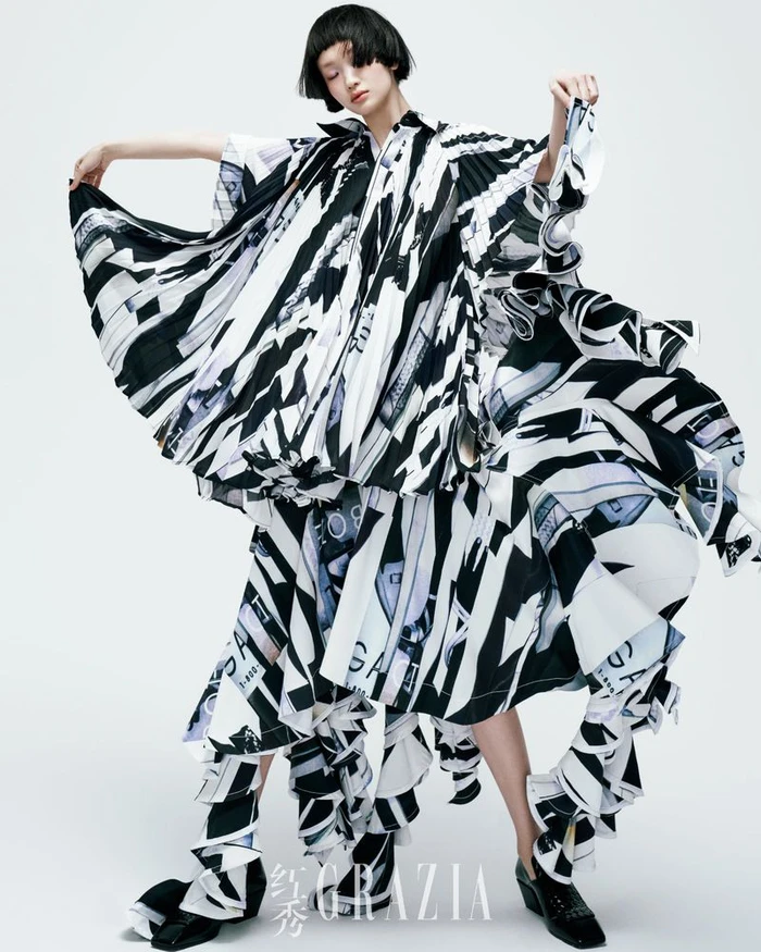 Model with short black hair wearing a black and white printed dress against white background