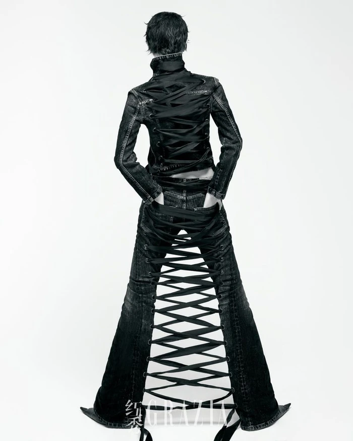 Model photographed from behind wearing a black laced denim jacket and matching flared trousers against a white background.