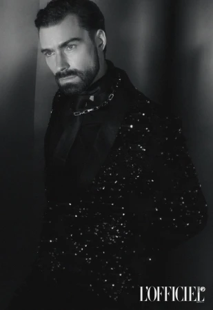 Black and white portrait of a bearded adult male wearing a sequined jacket in a low-key lighting environment against a dark wall.