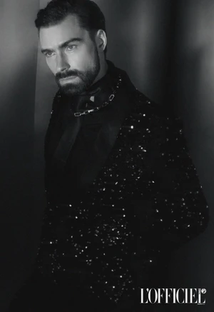 Monochrome portrait of a bearded man wearing a dark sequined blazer and chain necklace for L'Officiel Baltics by photographer Den Bandilet.