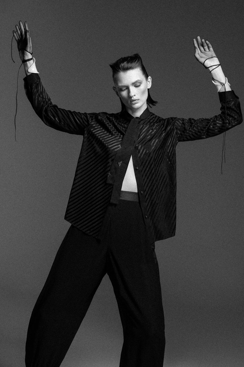 Model Lara Mullen in a black striped shirt and trousers posing against a grey seamless backdrop in a monochrome fashion editorial.