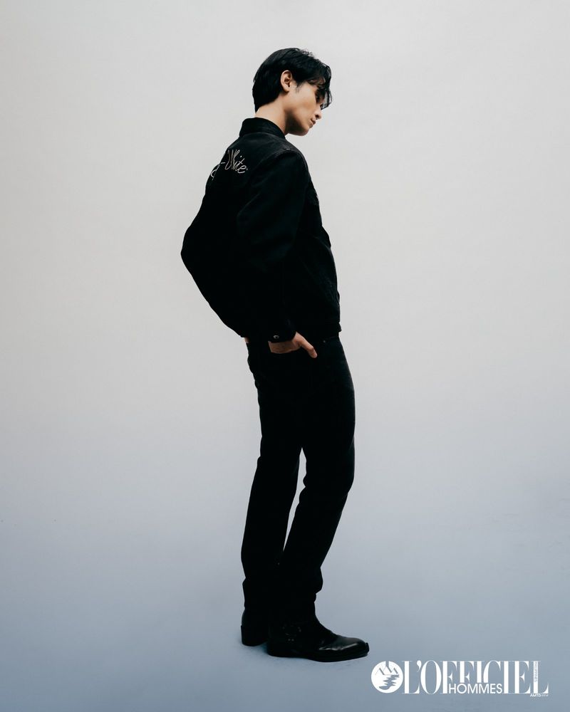 Man wearing a black jacket and pants standing against a pale grey studio background for L'Officiel Philippines.