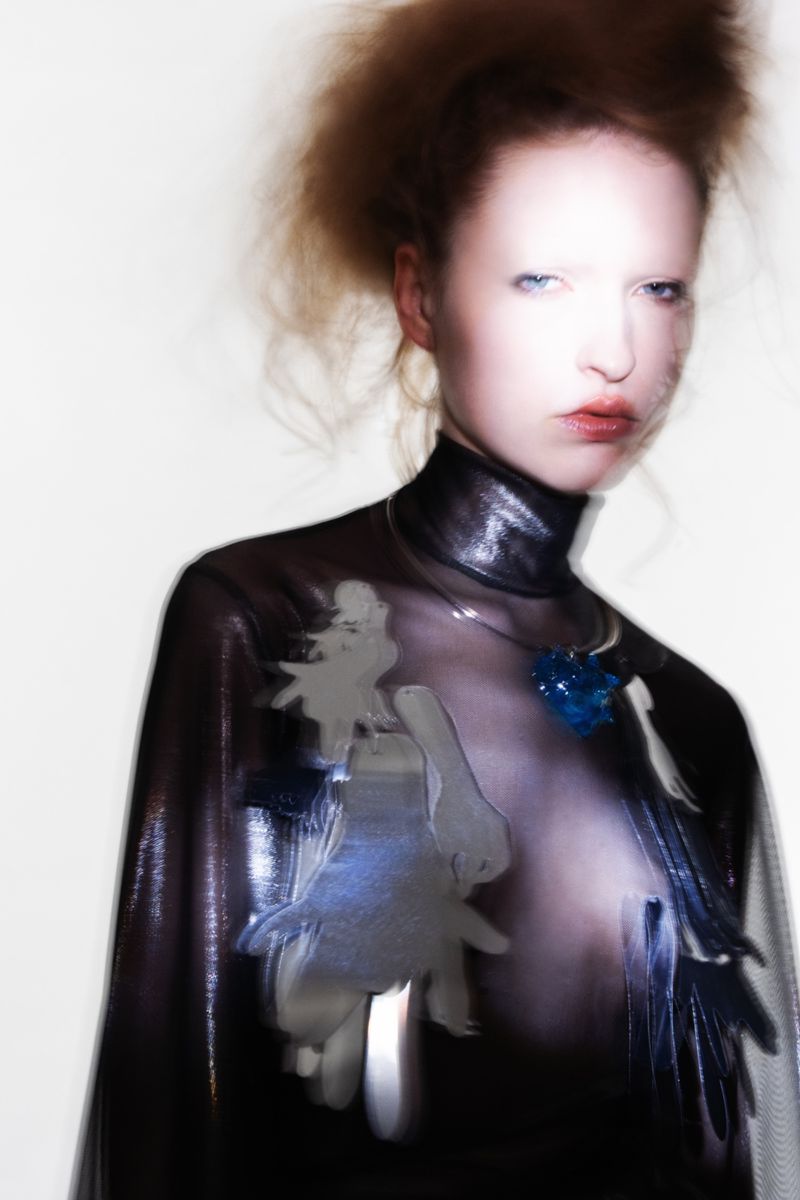High fashion close-up portrait of a woman with soft focus in a metallic high-neck top with dress designs against a white background.