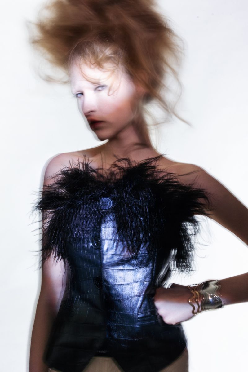 Woman in dark corset poses in front of white background with diffused studio lighting. Editorial fashion shot with hair and makeup.