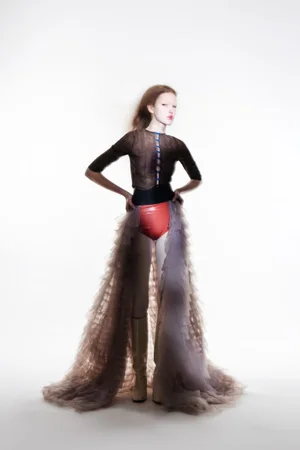 Model wearing dark sheer top, red briefs and layered tulle skirt against white background