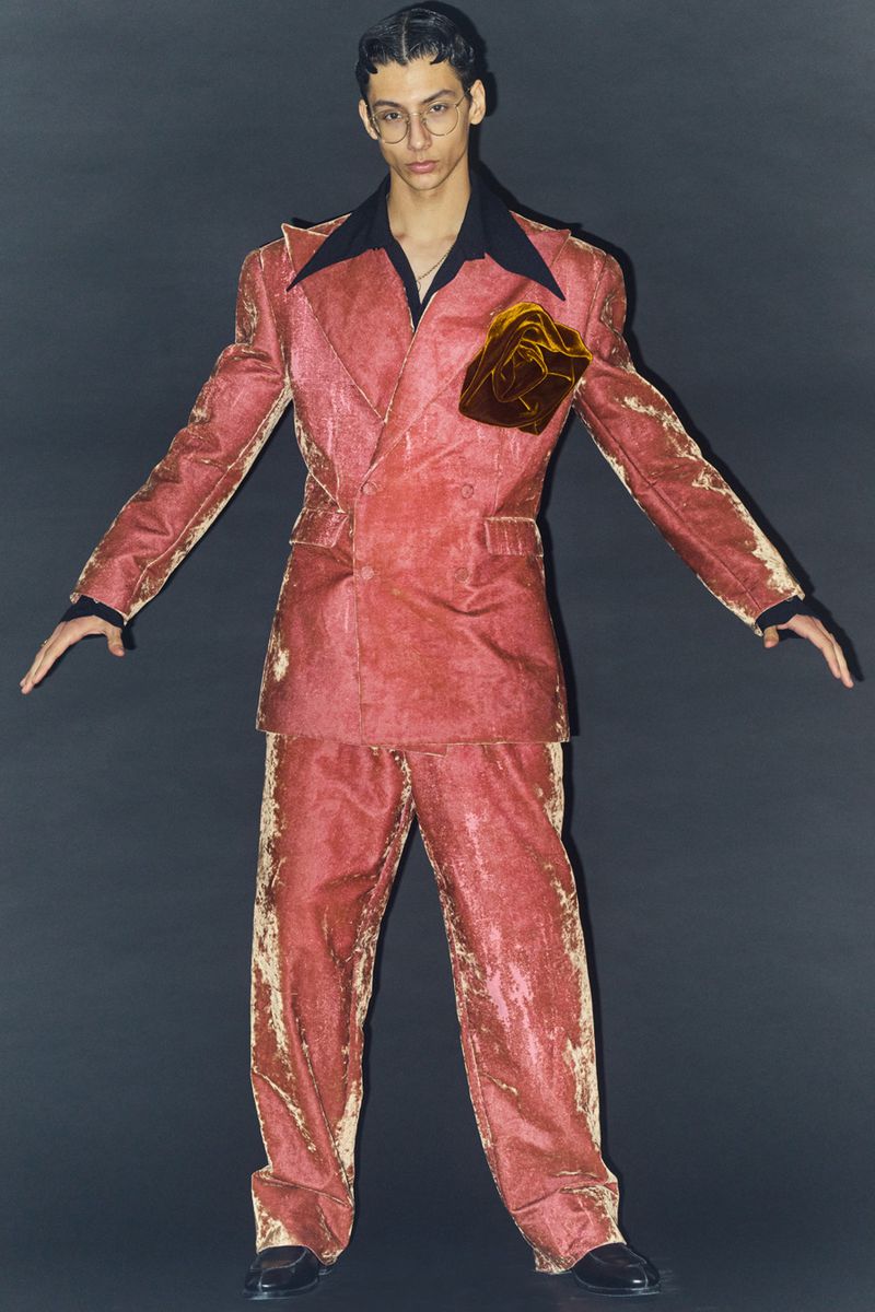Model wearing a textured red double-breasted suit standing against a dark seamless backdrop for HERO Magazine.