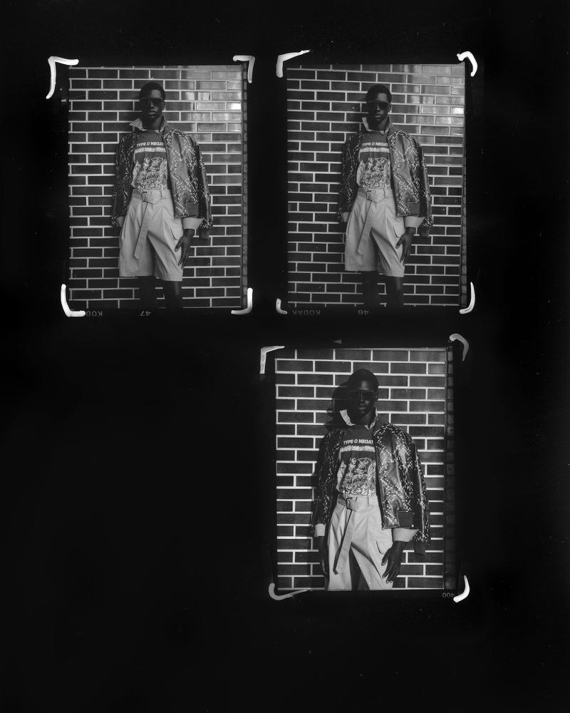 Three black and white photographs of a dark-skinned male wearing a patterned jacket and pants, standing in front of a brick wall.