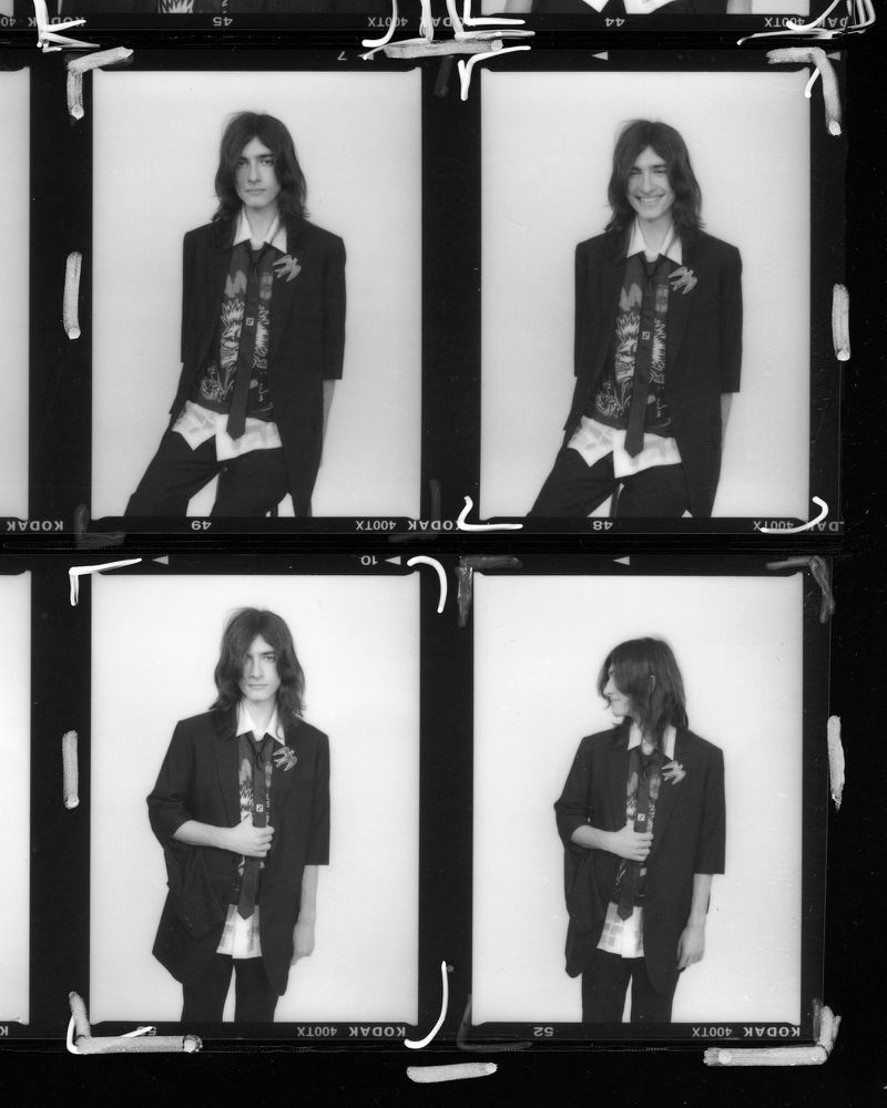 Black and white film strip displays four frames of a person in a blazer, tie, and shirt, posing in front of a bright background.