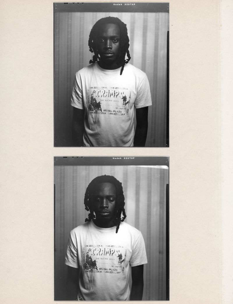 Monochrome portrait of a young adult with dark hair and a white T-shirt with text and graphics, captured in a film photograph.