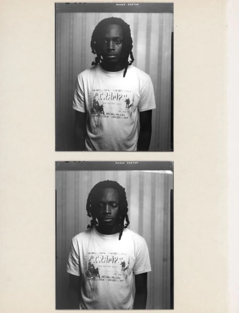 Monochrome portrait of a young adult with dark hair and a white T-shirt with text and graphics, captured in a film photograph.