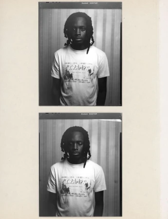 Monochrome portrait of a young adult with dark hair and a white T-shirt with text and graphics, captured in a film photograph.