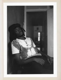 Portrait of Sam Akpro leaning against a wall wearing a t-shirt in a domestic interior for HERO Magazine