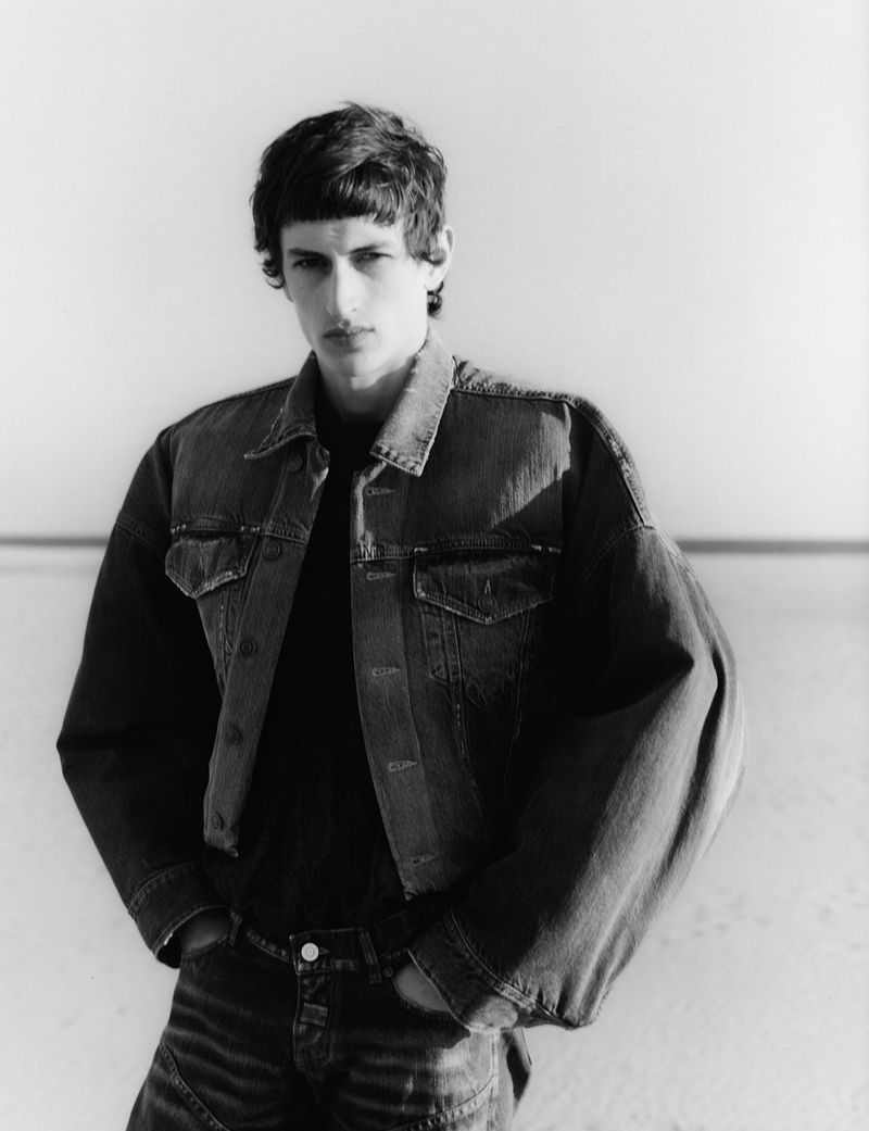 Monochrome portrait of a young male model wearing an oversized denim jacket against a bright seamless background.