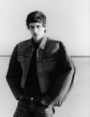Monochrome portrait of a young male model wearing an oversized denim jacket against a bright seamless background.